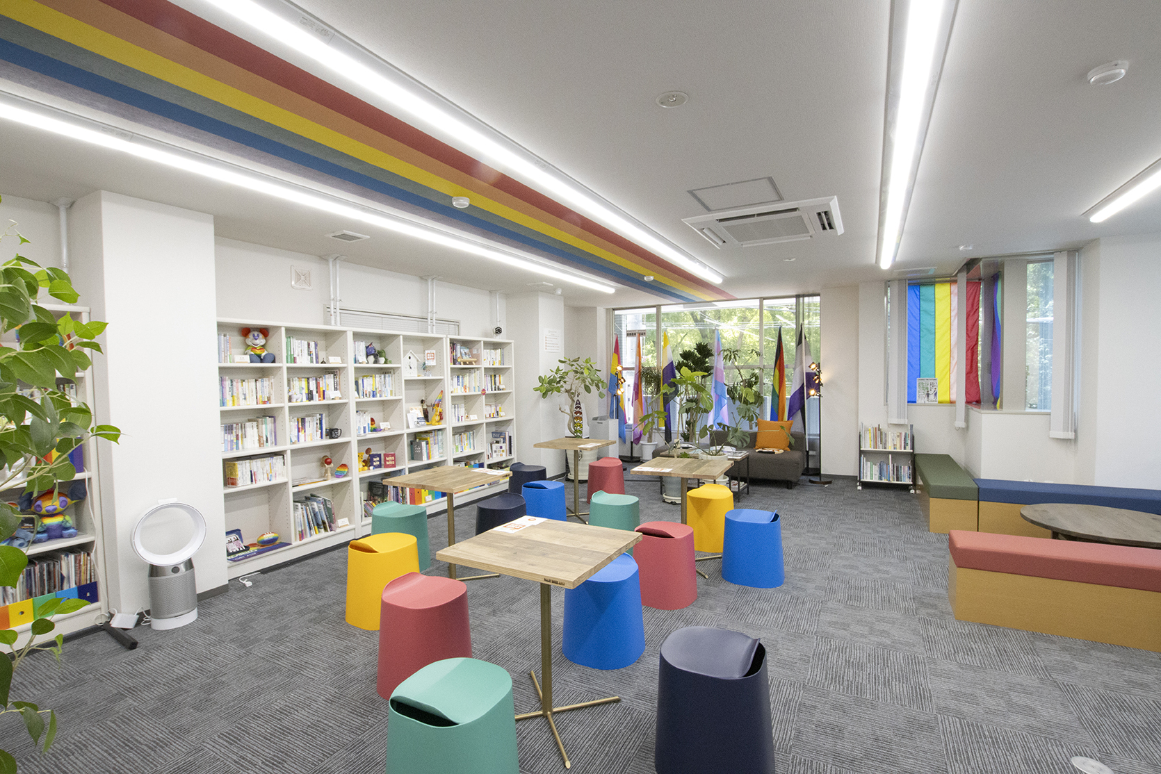 Intérieur de PRIDE CENTER OSAKA, avec bibliothèques, tables, sièges colorés et drapeaux arc-en-ciel.
